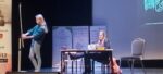 Aktorzy na scenie podczas przedstawienia - dwie aktorki, jedna siedzi w szkolnej ławce, druga stoi przy tablicy.