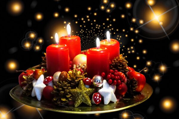 Zdjęcie przedstawiające 4 czerwone zapalone świece, obok na podstawce ozdoby Bożonarodzeniowe. Tło ciemne z błyszczącymi na zloty kolor gwiazdami.