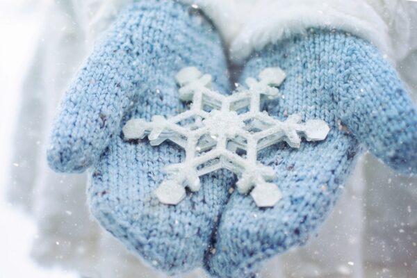 Grafika przedstawiająca zdjęcie dłoni w niebieskich rękawiczkach trzymających płatek śniegu.